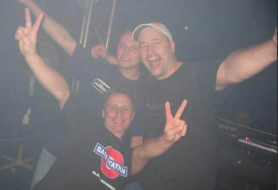 Three friends giving a peace sign, one wearing a Bass Station shirt