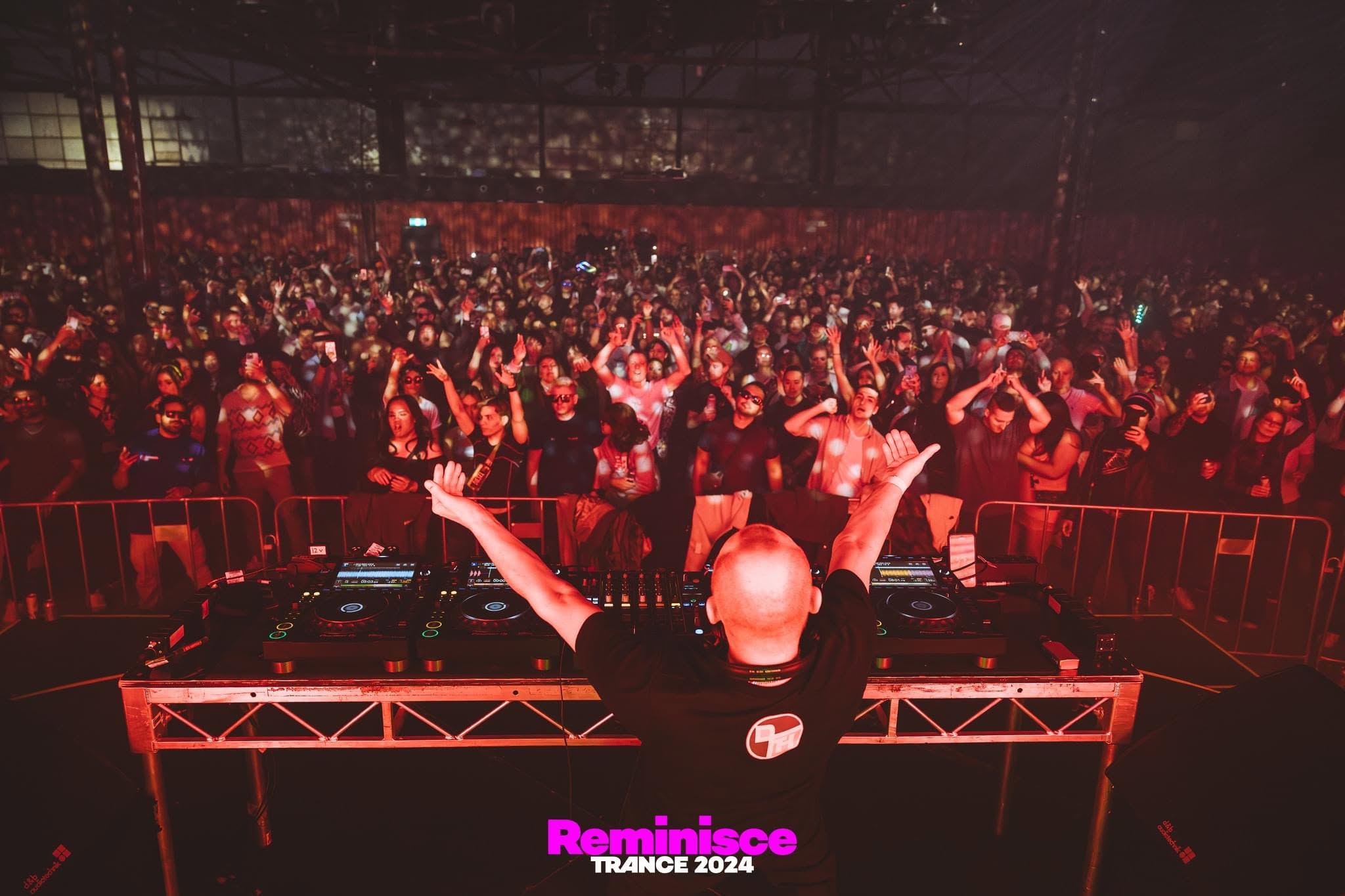 Jason Midro DJing to a packed crowd, arms raised, red stage lighting