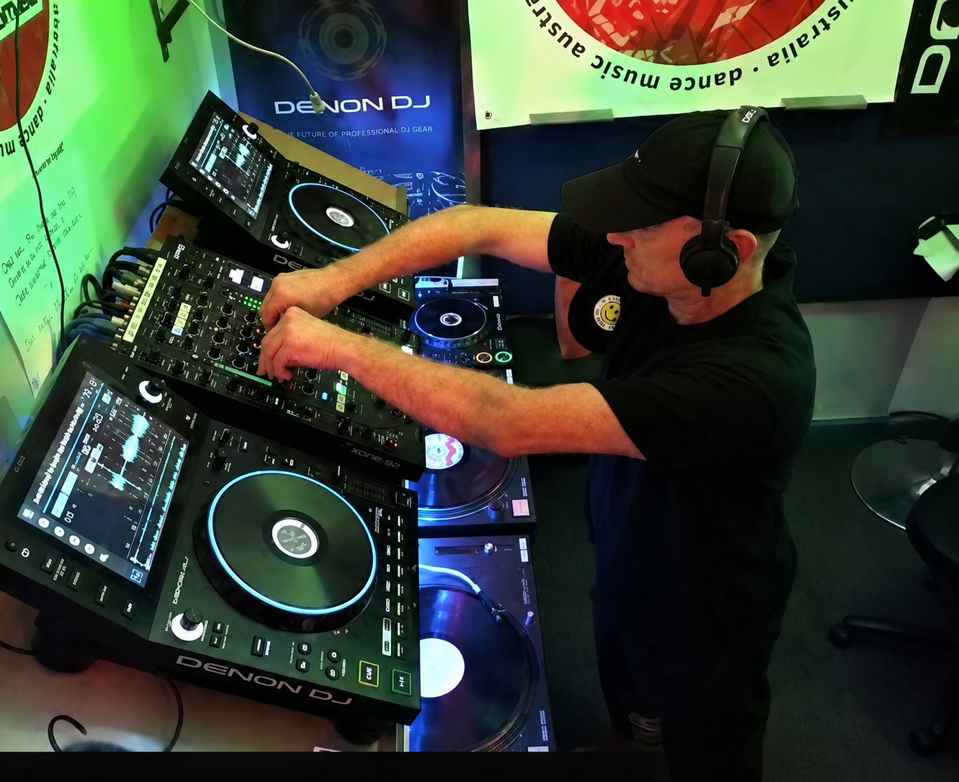 Jason Midro mixing on Denon DJ decks in the Dance Music Australia studio, KISS FM banner visible in the background